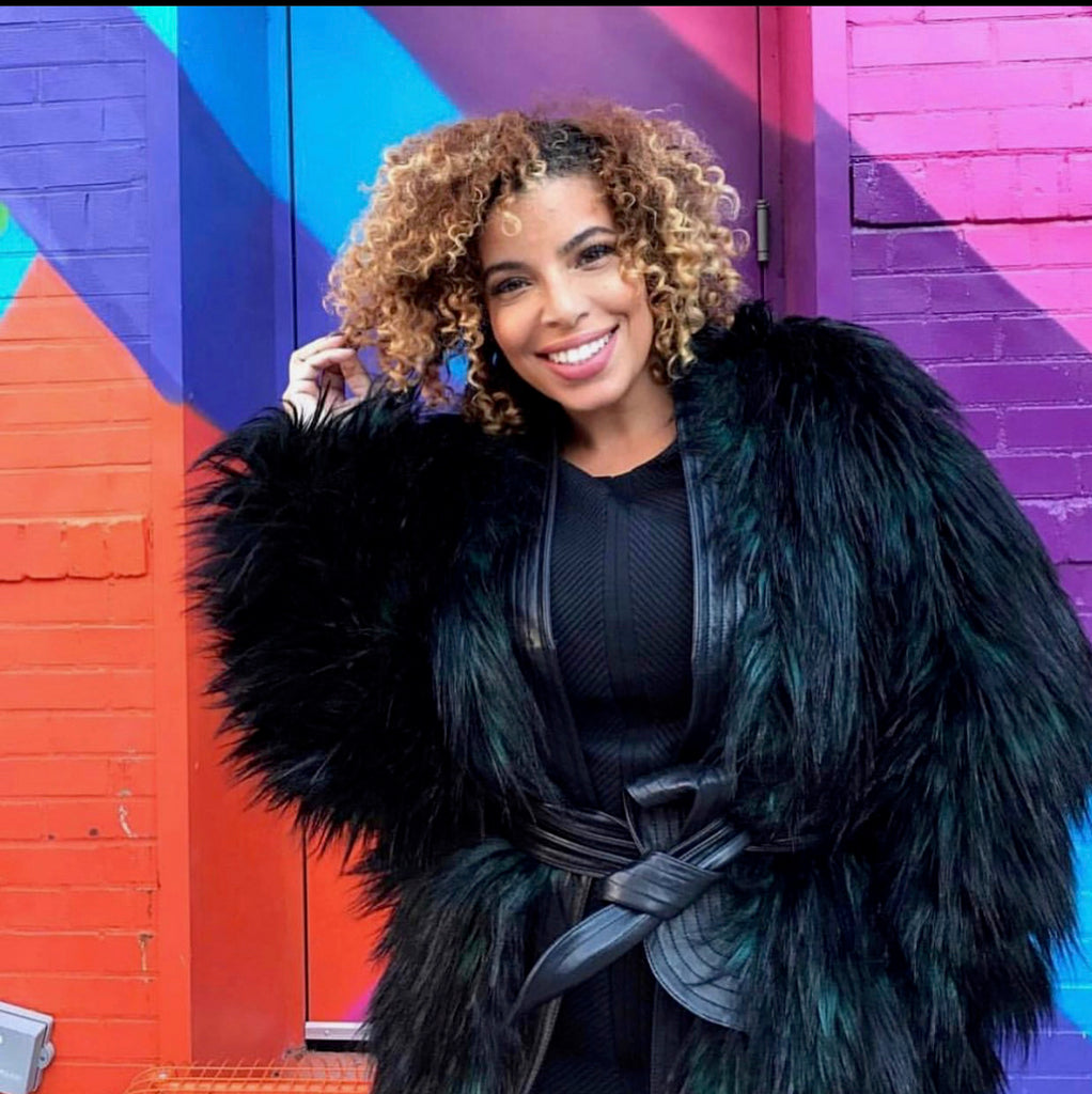 Celebrity Interior Designer, Neffi Walker smiling outside with bold colored brick background, wearing all black.